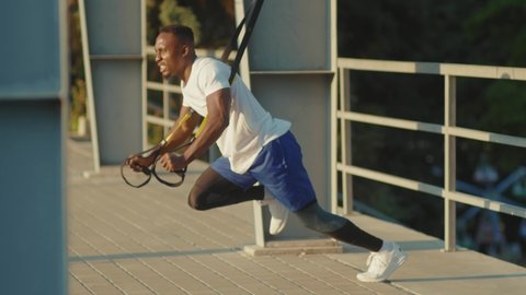 NEW YORK - September 5, 2020: Strong handsome african american guy working out with trx fitness rope outdoors body exercises at stadium muscular training sportswear sporty workout slow motion