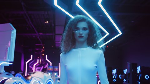 Beautiful caucasian woman in white futuristic costume and glasses walking in night club in city of future. Blue and violet neon light. Trendy stylish millennial female. VR club, future technology