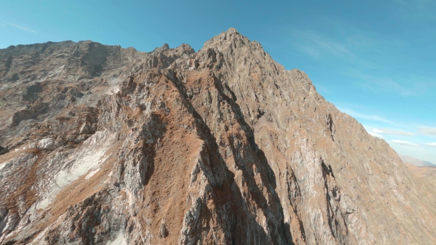 Fast extreme close diving drop down fly steep rocky mountain rock peak slopes and picturesque stone canyon with narrow winding creek on sunny day fpv racing drone first point aerial cinematic view. Royalty-Free Stock Footage #1062894319