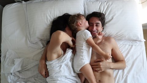 Casual parents and baby toddler in bed interaction, top view.