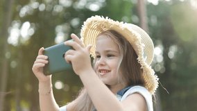 Happy smiling child girl watching in her mobile phone outdoors in summer.
