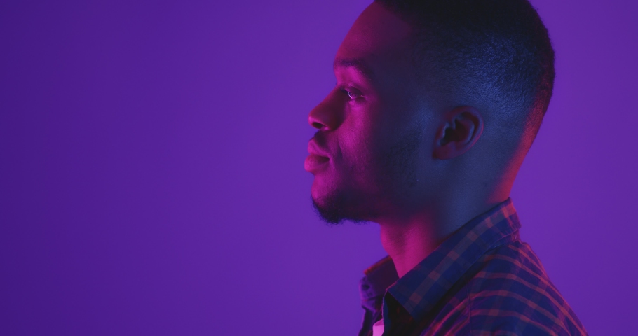 Side view portrait of young african american guy turning face to camera and laughing happily, neon lights, studio shot, empty space Royalty-Free Stock Footage #1062897355