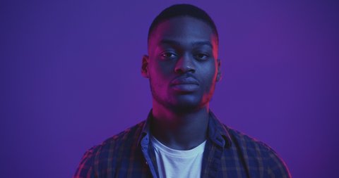 Close up portrait of serious confident african american guy turning face to camera and looking seriously in neon lights, studio shot