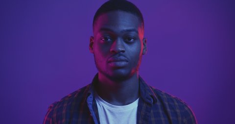 Profile portrait of young african american man turning to camera, looking seriously, studio shot in neon lights, close up