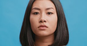 Close up portrait of shocked amazed asian woman touching face in astonishment and wonder, blue studio background