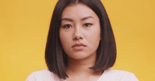 Studio portrait of unhappy depressed young asian woman pouting lips, looking sadly at camera, orange background, close up