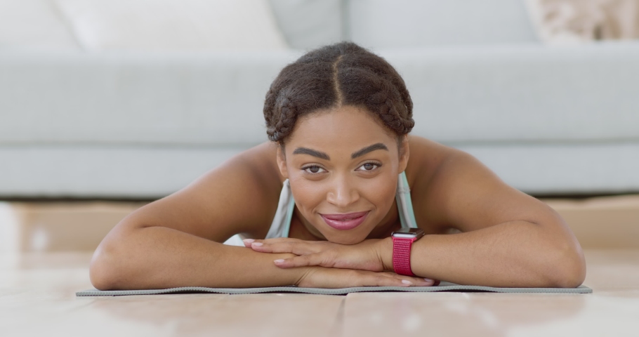 Portrait of young african american lady lying on mat after fitness training at home, smiling at camera