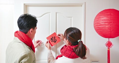 rear view of asian young couple stick character of word meaning luck on the door to celebrate new year - good fortune chinese calligraphy
