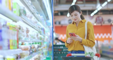 asian young business woman is searching information of products by smart phone at grocery store