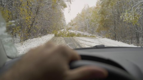 Person drives modern car along snowy rural road blocked with large fallen tree branch in forest on cold winter day close view from inside salon