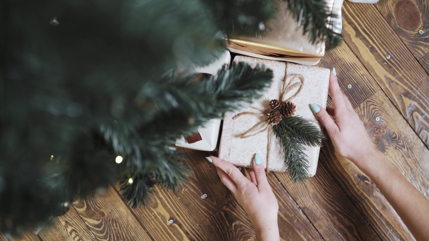 Top view of the hands of a woman who puts a present under the Christmas tree. New year surprise under the tree. High quality 4k footage