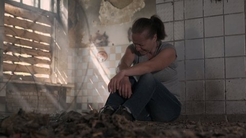 Depressed woman crying while sitting on floor in abandoned building alone.