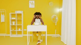 Young black woman with short curly hair is looking at camera and smiling, posing in creative yellow office, playing with marshmallow pieces, creative video concept, Slow motion.