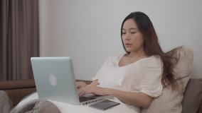 asian businesswoman in casual wear, working on laptop computer ans answering phone call on bed in bedroom. female entrepreneur work from home.
