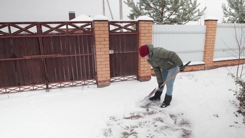 A woman with a shovel cleans snow covered path in backyard of house.