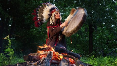 Shaman woman playing her shaman sacred drum at night in the forest. Ethnic traditions
