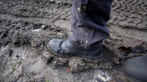 Worker in a working boots steps into the mud and leaves a footprint in mud