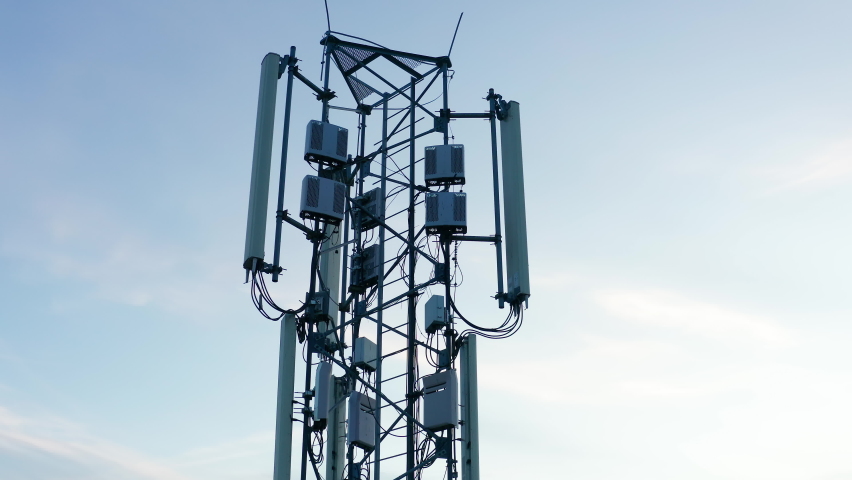 Telecommunications tower carrying broadcasting antennas for gsm, 3G, 4G and 5G cellular networks. Aerial drone shot of a tall metal structure with equipment for mobile telephony and internet. Royalty-Free Stock Footage #1062921574