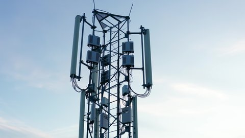Telecommunications tower carrying broadcasting antennas for gsm, 3G, 4G and 5G cellular networks. Aerial drone shot of a tall metal structure with equipment for mobile telephony and internet.