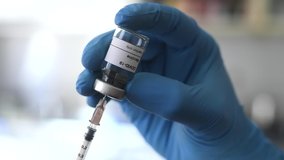 Close up of hand covered by medical blue gloves filling a syringe with liquid from a vial with a label reading Covid-19 vaccine - Powered by Shutterstock - Get 15% off with code: PIKWIZARD15