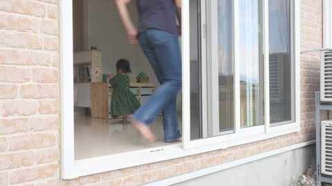 Happy Asian father and 2 years old daughter chase each other in the house. Japanese little toddler baby girl holding plush dog. Go round and round. Living room seen from the outside