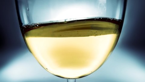 Creative macro slow motion video of white wine splashing in a glass from side to side like waves. Glass with splashing wine close-up.