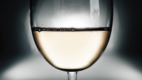 Creative macro slow motion video of white wine in a glass and a falling drops of wine. A glass with a slowly falling drops of wine close-up. Old retro grunge vintage style soft faded.
