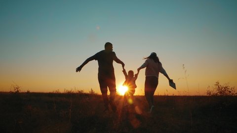 Happy young family together with their little child at sunset. People silhouettes on summer sunset meadow. Concept of friendly family.