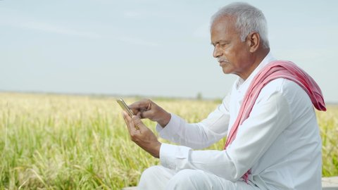 Indian famer using mobile at agricultural farm land - elder villager using phone - Concept of senior rural people using technology and smartphone