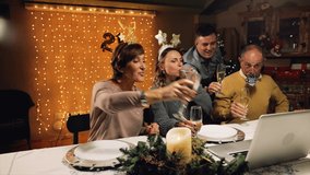 Funny and excited family greeting their relatives on New Years Eve, with a video call, toasting with champagne glasses. Online communication during Coronavirus Pandemic year, 2020-2021.