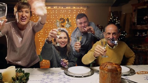 Tracking shot of excited family toasting with champagne for New Year's 2021, looking at camera. POV of a friends video call. Concept of social distance due to coronavirus, Covid-19 pandemic.