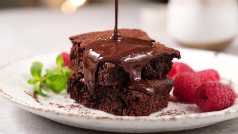 Chocolate syrup pouring on chocolate brownies. Tasty dark rich brownies served with raspberries
