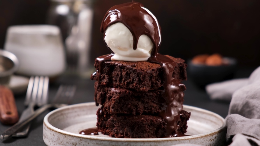 Chocolate brownies with vanilla ice cream and chocolate syrup. Syrup pouring on ice cream on brownies. Rich in sugar high calorie sweet food | Shutterstock HD Video #1062937669