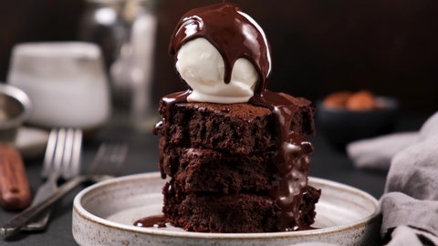 Chocolate brownies with vanilla ice cream and chocolate syrup. Syrup pouring on ice cream on brownies. Rich in sugar high calorie sweet food