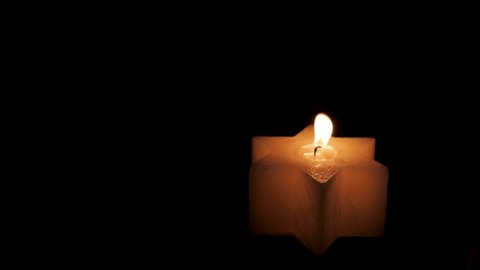 A lighted Jewish yellow candle in the shape of a star of David on Hanukkah. On a black isolated background close up in 4K without faces of people.