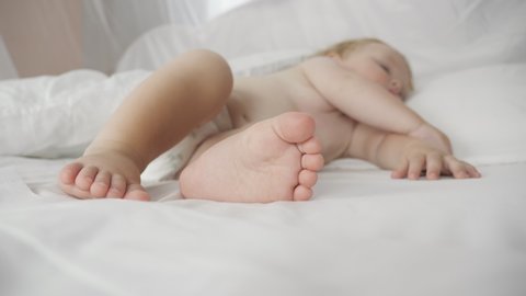 Baby sleeping sweetly in a comfortable bed. Little feet of a newborn baby. Child feet skin in close-up. Handheld shot, selective soft focus.