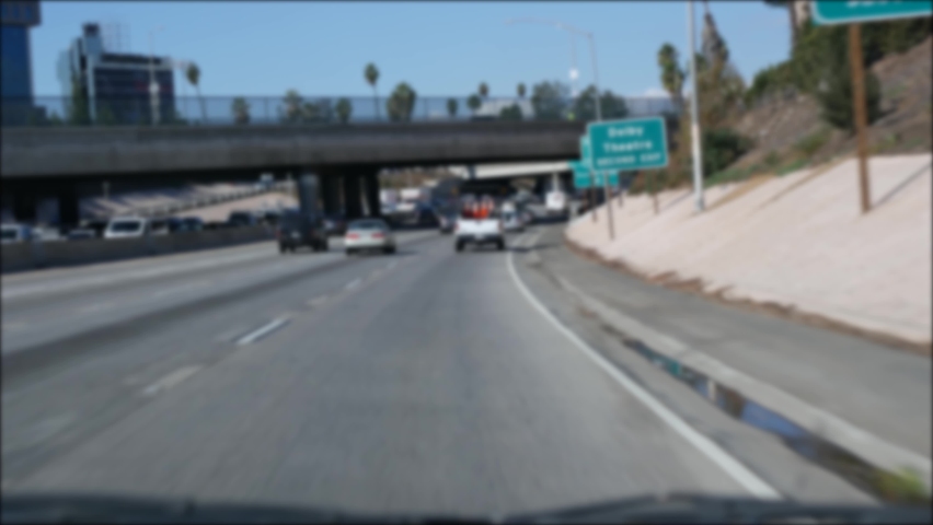 Driving on intercity freeway in Los Angeles, California USA. Defocused view from car thru glass windshield on busy interstate highway. Blurred suburb multiple lane driveway. Camera inside auto in LA. Royalty-Free Stock Footage #1062939880
