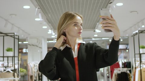 Young pretty woman is taking a selfie at clothing store, static shot, close up