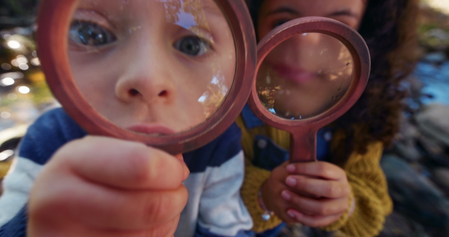 Small boy and girl looking at camera with magnifying glass