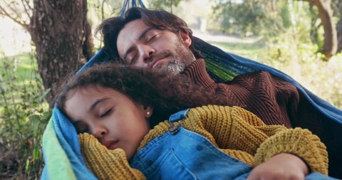 Father and daughter sleeping on a hammock in the woods