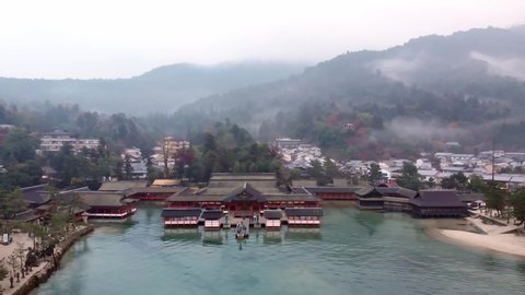 Aerial descending above the historical floating gate of Itsukushima Shrine on a lake in a small Japanese town on a foggy day