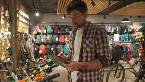 Young Caucasian male seller holding presentation of bicycles goods to buyer, first-person view, professional store of sporting and travel goods. Buying equipment and quality service from professionals