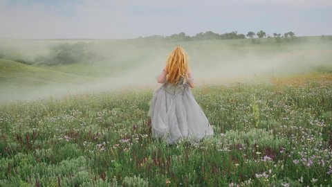 young happy fantasy blonde woman queen runs, walks in green nature, whirls, dances fluttering skirt, gray dress waving in motion. Vintage summer clothes. Candid girl princess bride. Back rear view