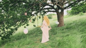 young happy blonde woman walks in green nature, whirls, dances fluttering skirt, silk pink dress waving in motion. Vintage summer clothes. Rustic style wedding modern candid girl bride. Back rear view