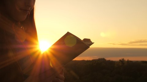 A person reads a book in the sun. Man reads Bible outdoors. A man holds Bible in his hands and studies the word of God at sunrise on top of mountain. Searching for truth in scriptures.