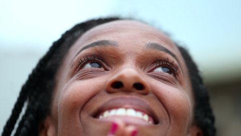 Black woman opening eyes looking up to sky with smile. Hopeful African person