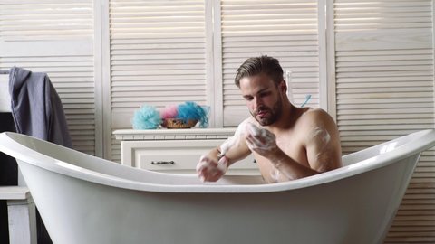 Confident guy with shaver in bathroom. Bath concept. Young guy bathing in the bath in bathtube. Gay concept. Male beauty, Care body and skincare concept