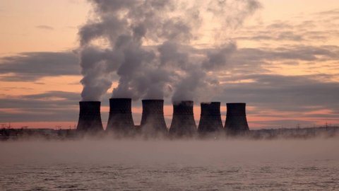 Nuclear power plant turbines pollute the environment and release chemicals into the atmosphere at sunset. Birds crows fly over the turbines