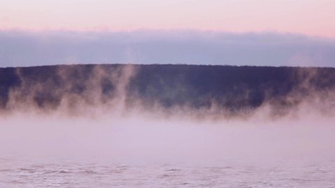 Steam floats over the water at dusk after sunset. Evaporation of water over the river, thick fog