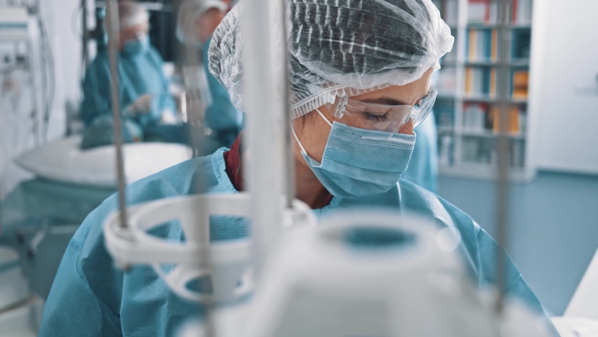 Indoor portrait young caucasian woman medical worker doctor professional nurse therapist wearing respiratory mask and blue uniform working in operating room. Royalty-Free Stock Footage #1062955684